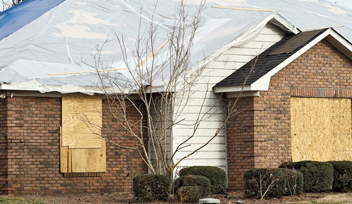 House with a large tarp covering the roof, boarded-up windows